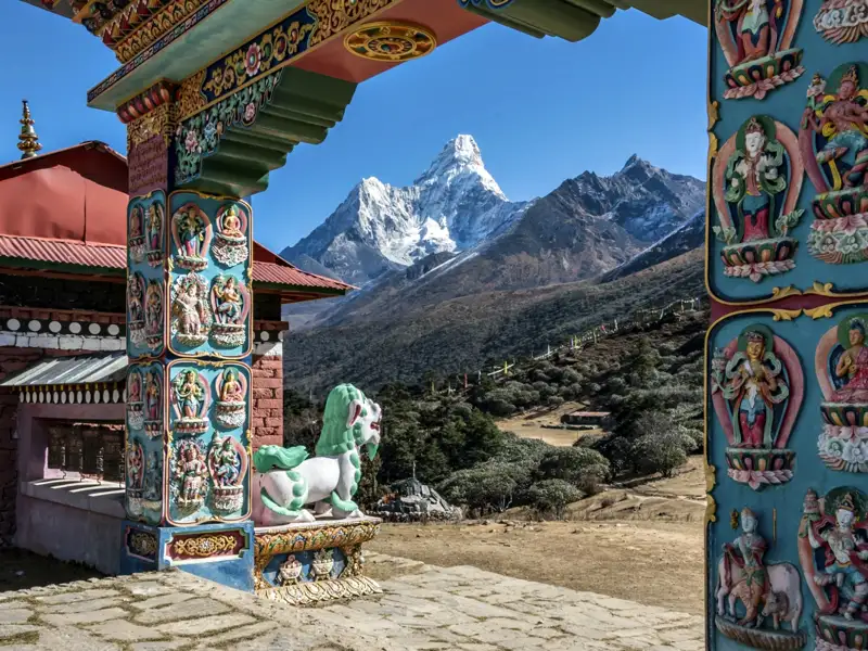 Blick durch ein kunstvoll verziertes Tor eines buddhistischen Tempels auf die schneebedeckten Himalaya-Gipfel.