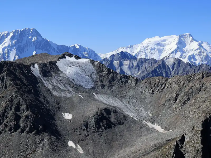 Ein Gletscher inmitten einer bergigen Landschaft mit schneebedeckten Gipfeln im Hintergrund.