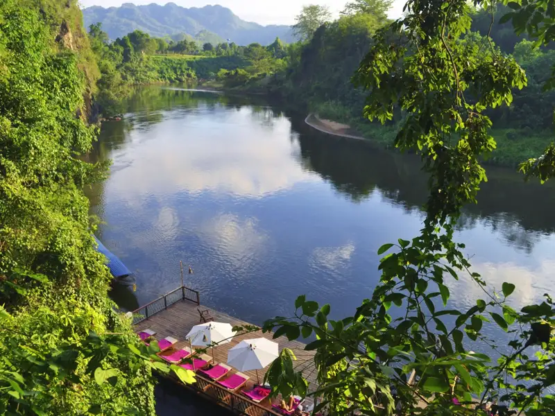Entspannungsbereich am Fluss mit Liegestühlen und Sonnenschirmen.