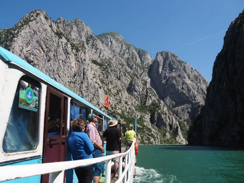 Ausflugsboot mit Passagieren fährt durch eine Schlucht mit hohen, steilen Felswänden und türkisgrünem Wasser.
