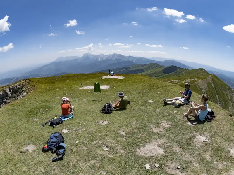 Wanderer ruhen sich auf einem Berggipfel aus und genießen den Panoramablick auf die Berglandschaft.