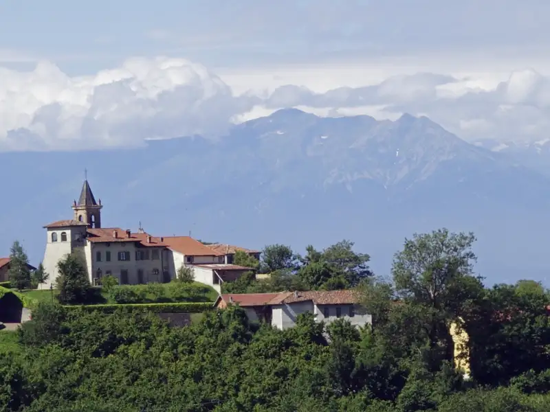 Panoramablick auf ein italienisches Bergdorf mit Kirche und Alpenpanorama.