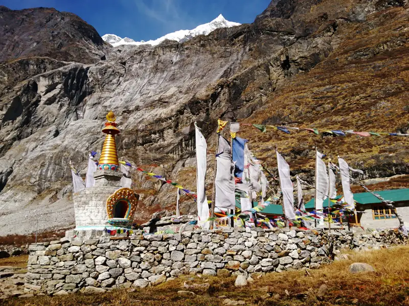 Gebetsfahnen und ein Stupa vor einer Berglandschaft.