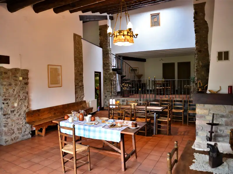 Speisesaal mit Steinwänden, Holzbalken und gedecktem Tisch.
