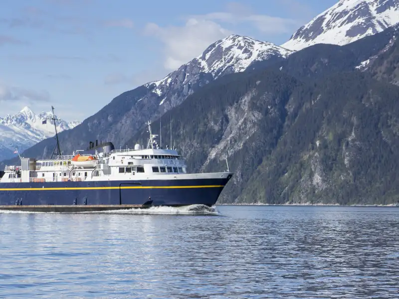 Fähre auf dem Wasser vor schneebedeckten Bergen.