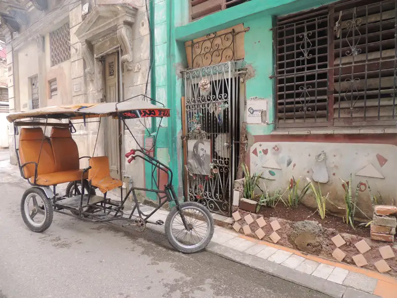 Ein Fahrradtaxi, ein typisches Transportmittel in Kuba, parkt vor einem bunten Haus.