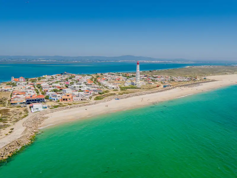 Luftbild der Küste mit Leuchtturm, Strand und türkisfarbenem Wasser.