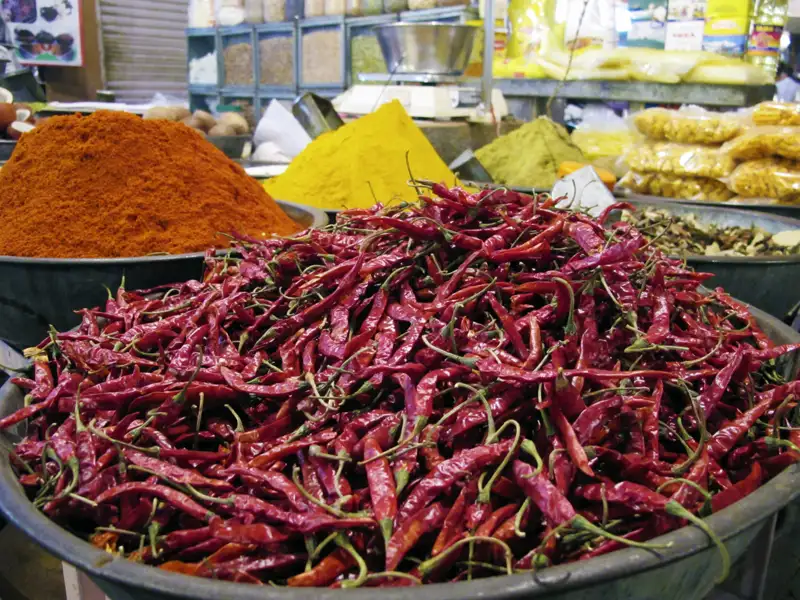 Getrocknete rote Chilischoten in einer Schüssel auf einem Markt, umgeben von anderen Gewürzen.