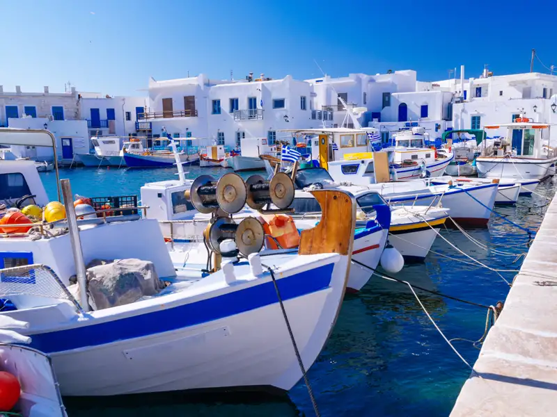 Traditionelle griechische Fischerboote im Hafen, festgemacht am Kai, vor dem Hintergrund der typischen weißen Architektur.