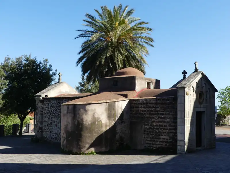 Historische Kapelle mit Steinfassade und Palmen.
