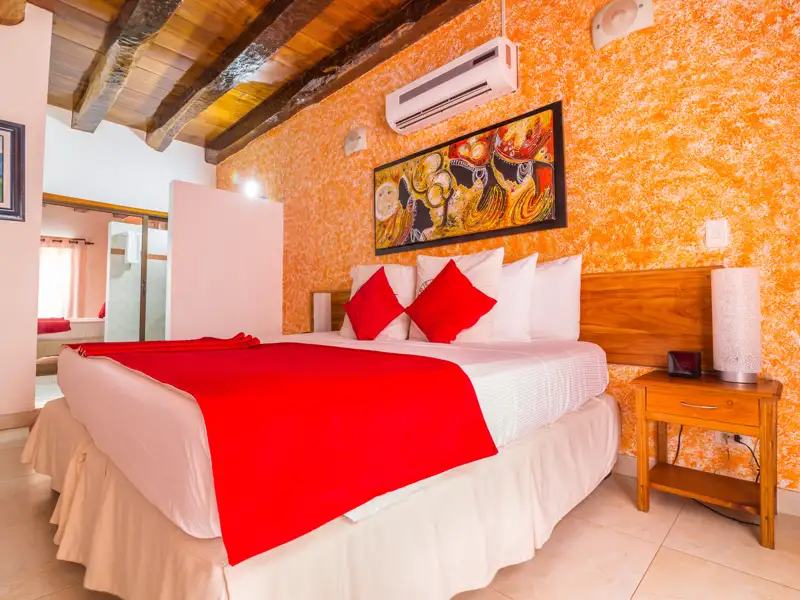 Schlafzimmer mit roter Tagesdecke, orangen Wänden, Klimaanlage und Nachttisch.
