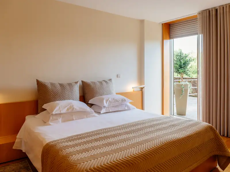 Schlafzimmer mit Doppelbett, Kissen und Zugang zum Balkon.