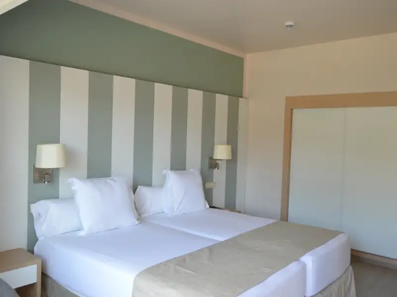 Zwei Einzelbetten in einem Hotelzimmer mit gestreiften Wänden und einem Kleiderschrank.