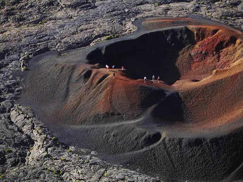 Wanderer erkunden den Rand eines Vulkankraters mit unterschiedlichen Farbschattierungen im Gestein.