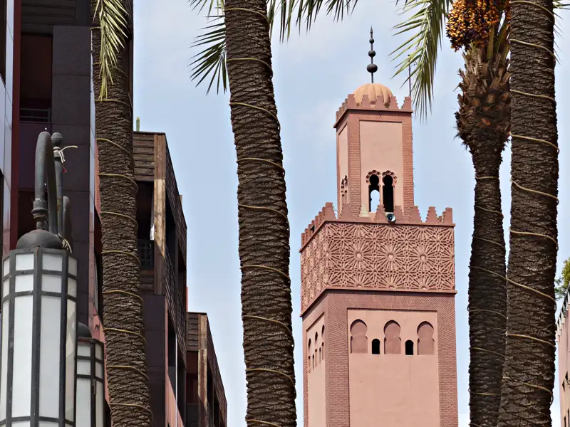 Minarett einer Moschee, teilweise verdeckt durch Palmenstämme.