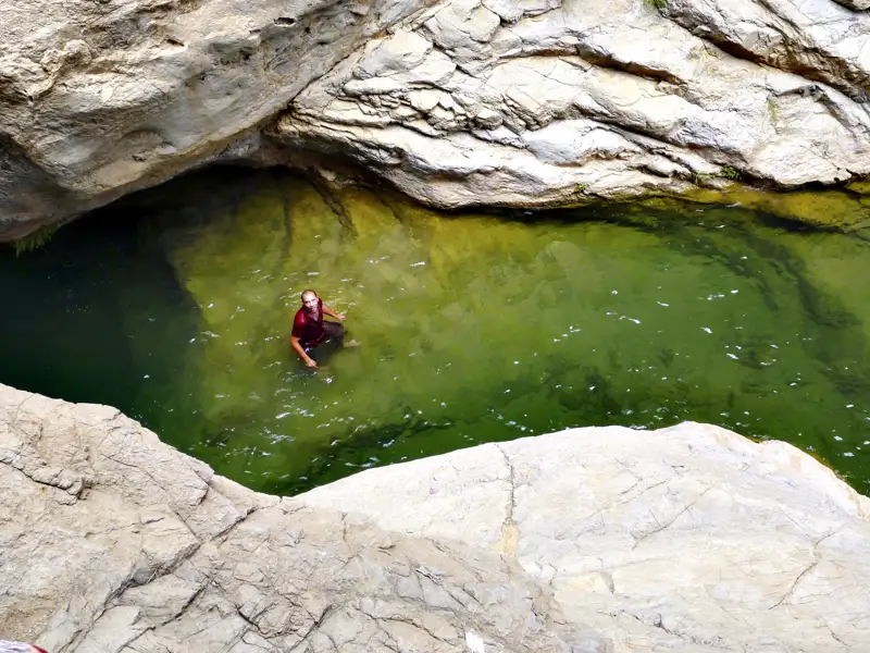 Eine Person erfrischt sich im Wasser eines natürlichen Pools inmitten einer felsigen Schlucht.