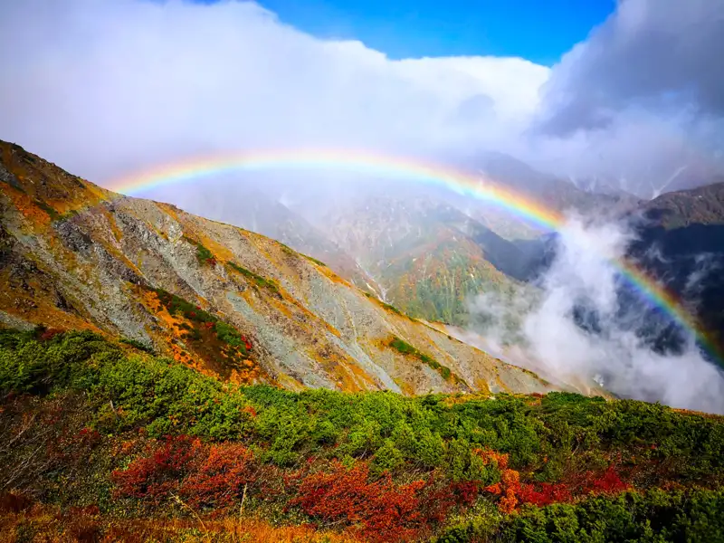 Regenbogen über herbstlichen Bergen.