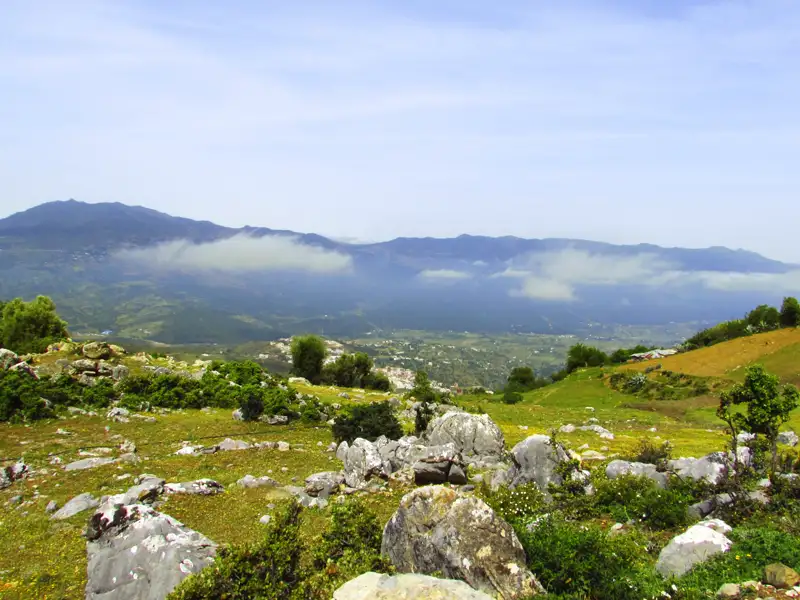 Panoramablick auf eine Berglandschaft mit Tal und Wolken.