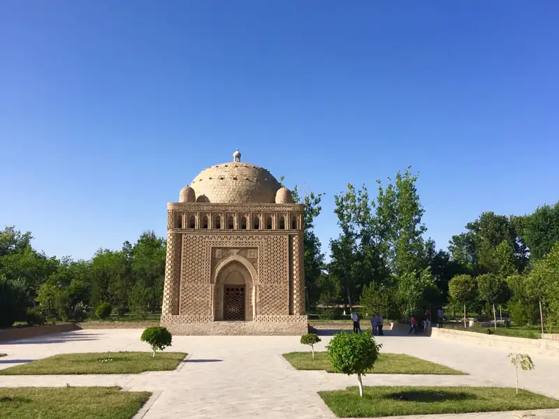 Historisches Mausoleum mit Kuppel und kunstvollen Verzierungen, umgeben von Bäumen und Wegen.