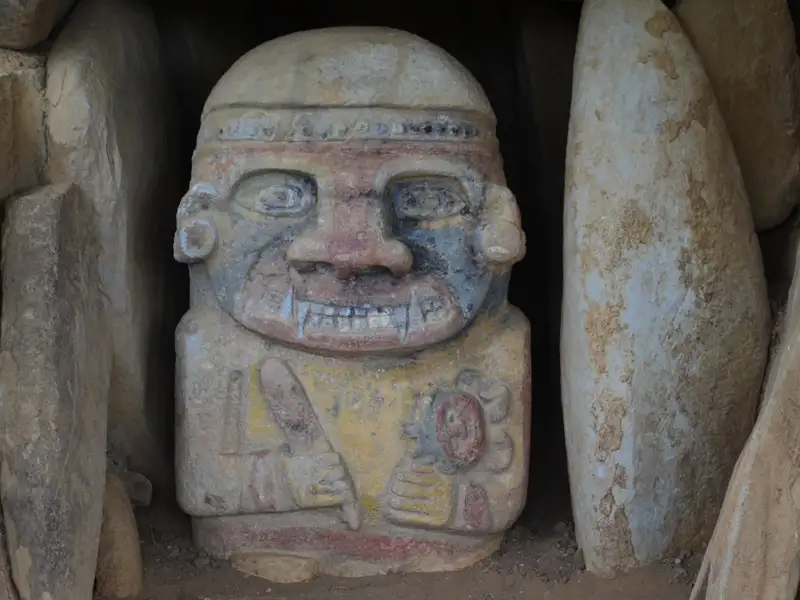 Antike Statue mit Bemalung und Verzierungen, gefunden in einer steinernen Umgebung.