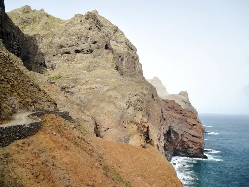 Schmaler Küstenpfad an steilen Klippen mit Blick auf das Meer.