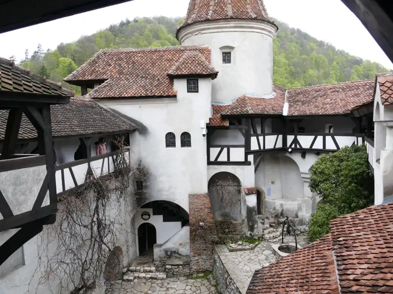 Blick auf den Innenhof der Burg mit seinen architektonischen Details wie den weißen Wänden, dem Fachwerk und den roten Ziegeldächern. Ein Brunnen befindet sich in der Mitte des Hofes.