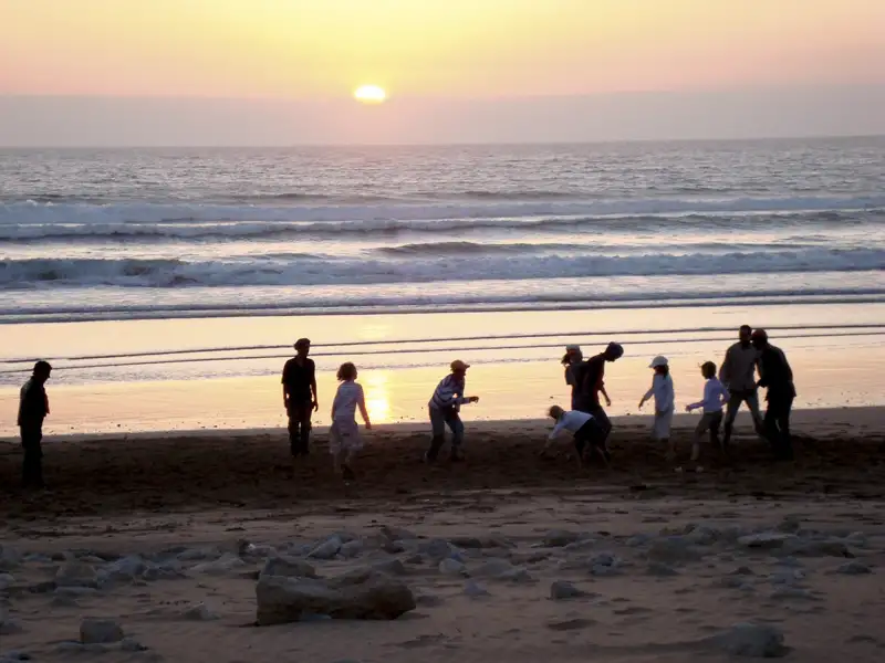 Sonnenuntergang am Strand mit spielenden Menschen.