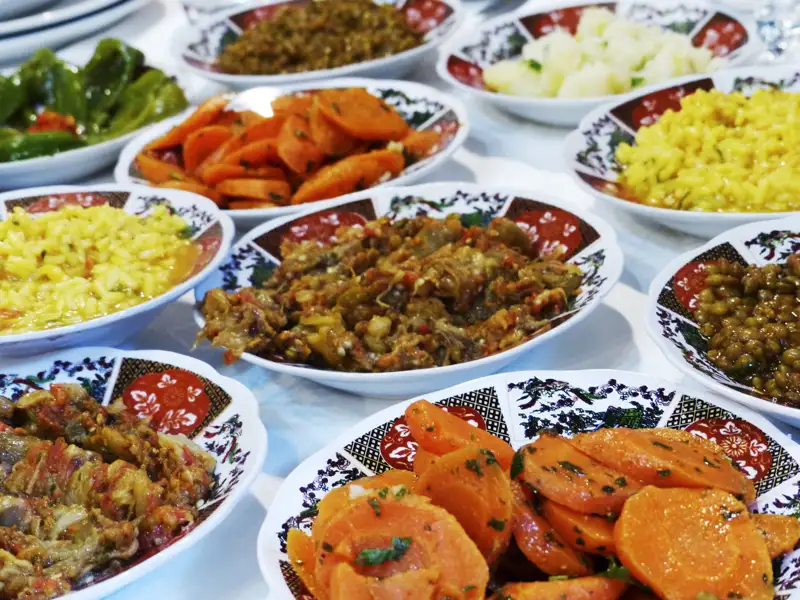 Eine Auswahl an marokkanischen Speisen, darunter gekochte Karotten, grüne Paprika, Reisgerichte und verschiedene Fleisch- oder Gemüse-Eintöpfe.