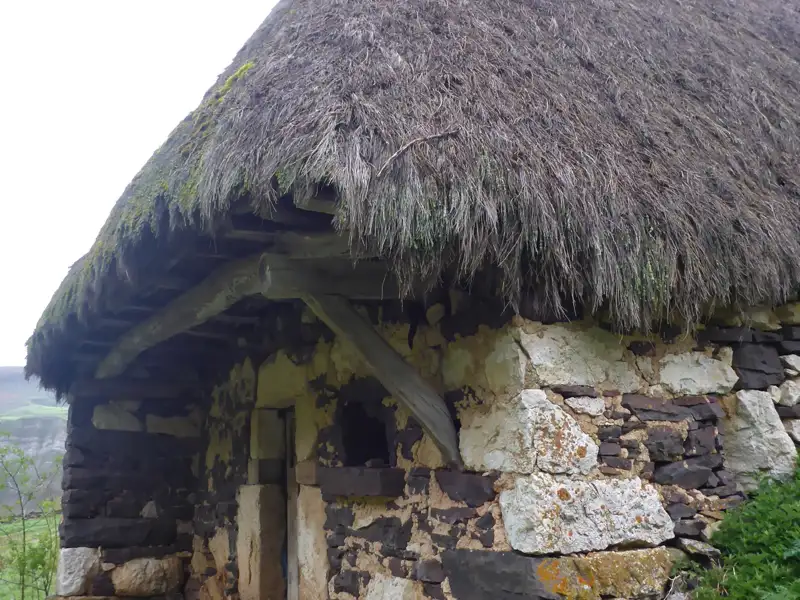 Reetdach und Steinmauerwerk einer historischen Hütte.
