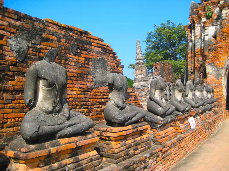 Verwitterte Buddha-Statuen vor einer Ziegelmauer in einer historischen Tempelanlage.