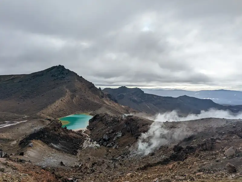 Türkisfarbener Kratersee und vulkanische Dämpfe in einer Berglandschaft.