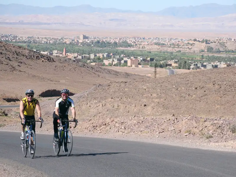Zwei Radfahrer auf einer Radtour durch eine Wüstenlandschaft. Sie nähern sich einer Stadt im Hintergrund.