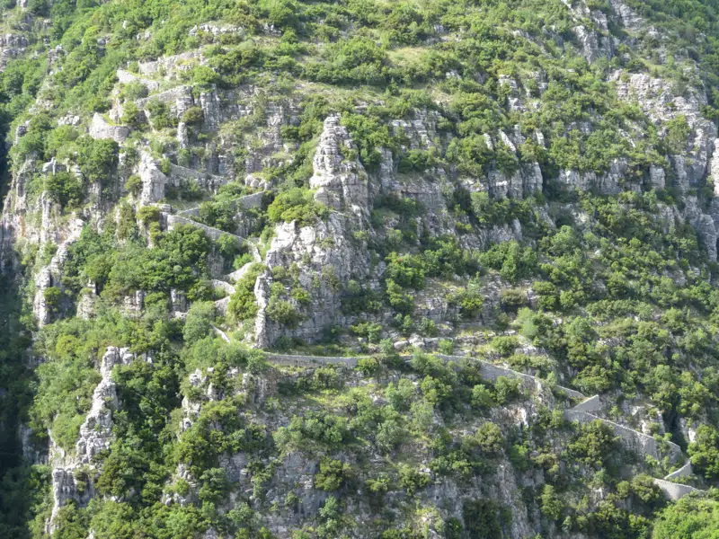 Gewundener Bergpfad durch Felsen und Vegetation.