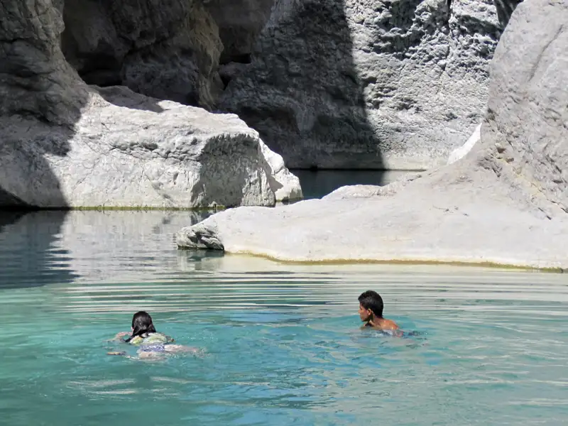 Zwei Personen schwimmen in einem natürlichen Pool zwischen Felswänden.