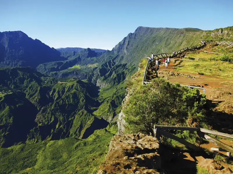 Wanderer genießen die Aussicht von einem Bergpfad auf ein üppiges grünes Tal.