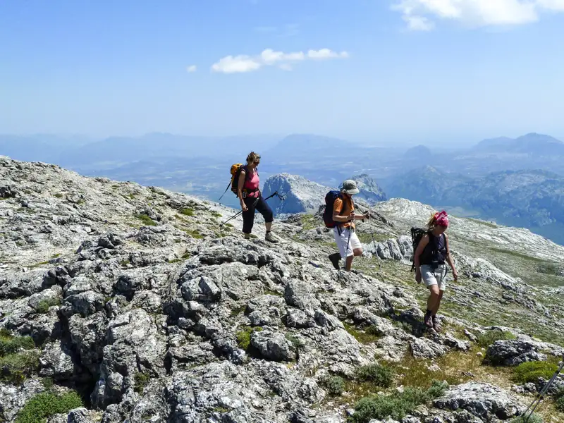 Drei Wanderer auf einem felsigen Bergpfad mit Blick auf die Berglandschaft.