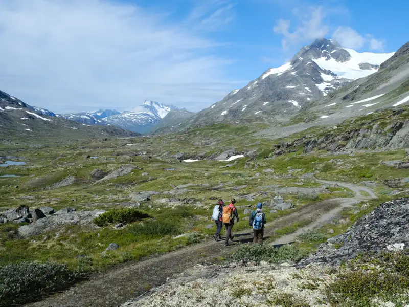 Drei Wanderer auf einem Bergpfad in einer Gebirgslandschaft.