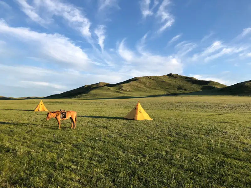 Pferd und Zelte in einer grünen Hügellandschaft.